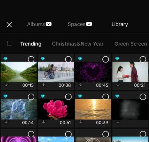CapCut Mobile media picker showing video clips with circular checkboxes in the top-right corner of each thumbnail. Select clips by tapping the circles; filled circles indicate selected items.